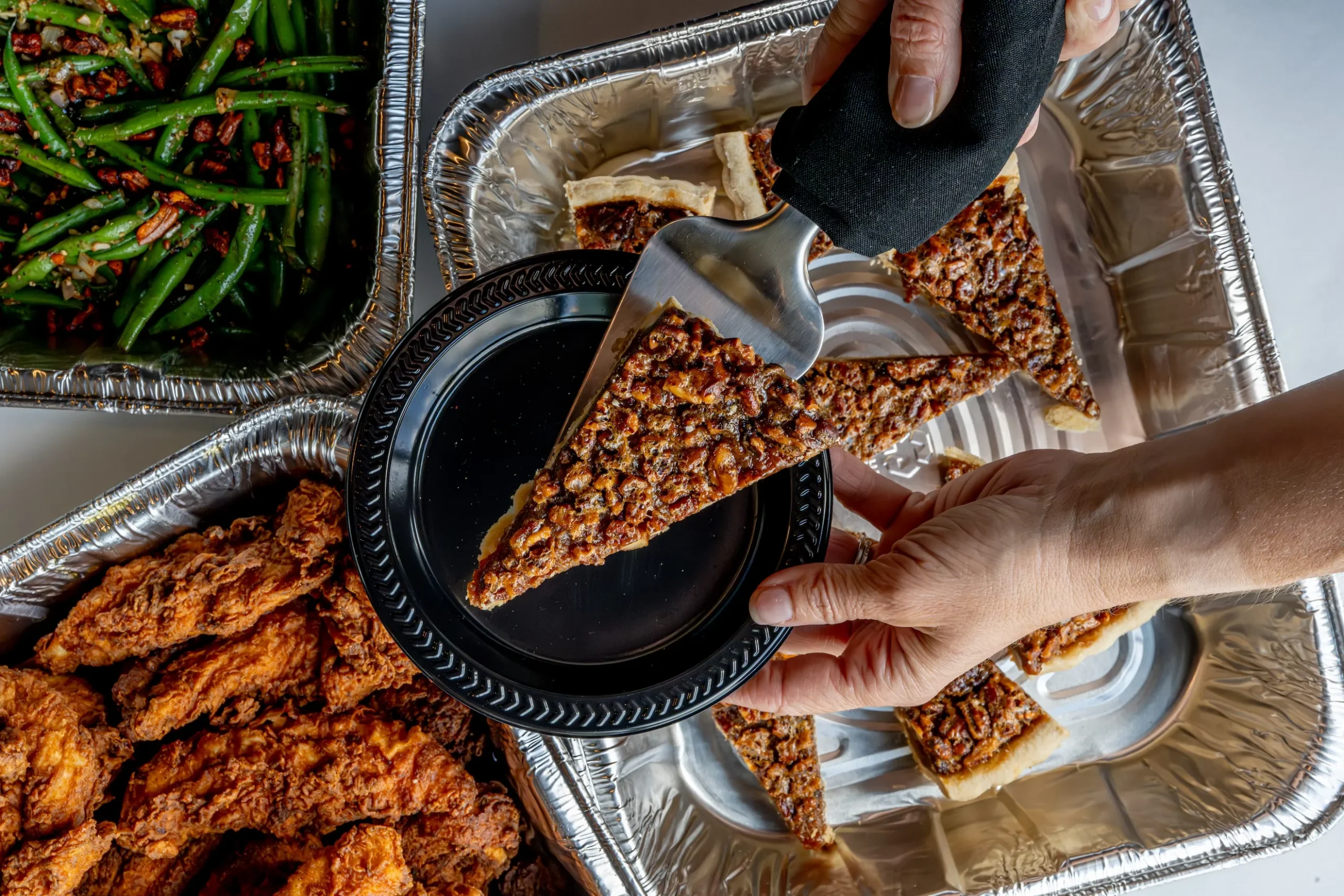 a piece of pecan pie on a plate next to chicken tenders and green beans